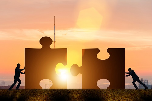 People at sunset pushing two pieces of a jigsaw together